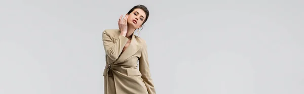 Young woman in fashionable clothes touching face while posing isolated on grey, banner — Stock Photo