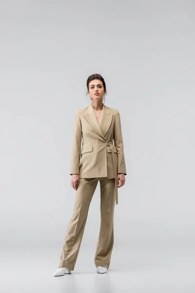 Full length view of woman in elegant suit looking at camera while posing on grey — Stock Photo