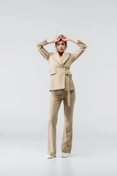 Full length view of fashionable young woman posing with hands near forehead on grey — Stock Photo