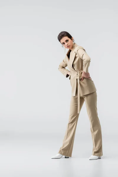 Trendy woman in beige pantsuit posing with hands on hips on grey — Stock Photo