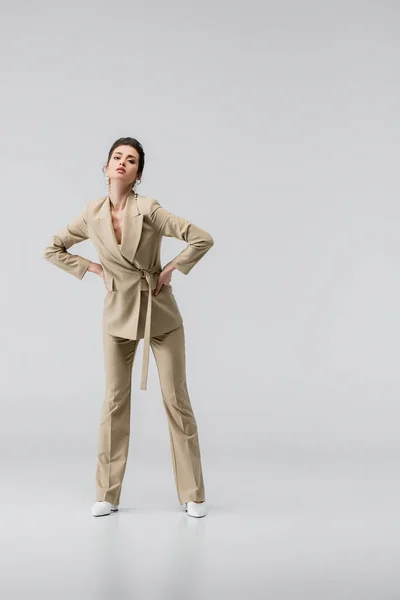 Full length view of sensual woman in elegant pantsuit posing with hands on hips on grey — Stock Photo