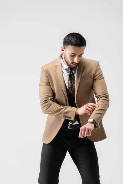 Uomo arabo alla moda controllando il tempo sull'orologio da polso mentre posa isolato sul grigio — Foto stock