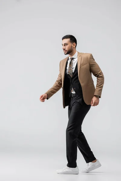 Вид на повну довжину модного мусульманського чоловіка в костюмі і кросівки, що ходять на сірому — стокове фото