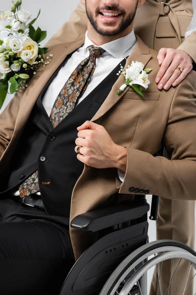Vista cortada de mulher com bouquet de casamento tocando ombro de noivo árabe com deficiência em cinza — Fotografia de Stock