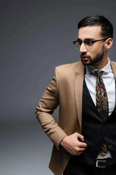 Joven árabe en blazer beige y chaleco negro mirando hacia otro lado en gris - foto de stock