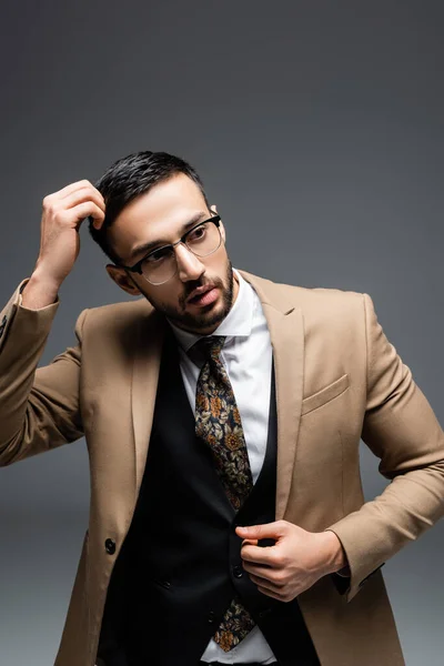 Hombre musulmán elegante tocando la cabeza mientras mira hacia otro lado en gris - foto de stock