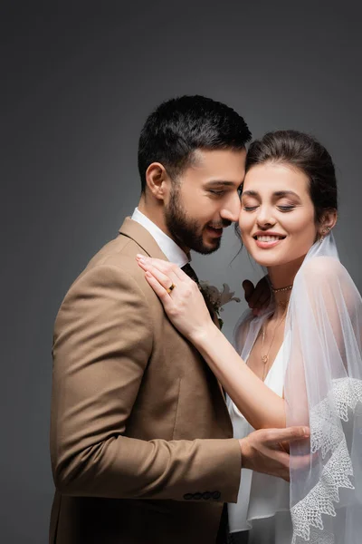 Happy bride with closed eyes near elegant muslim groom isolated on grey — Stock Photo
