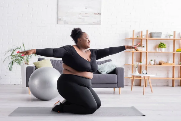 Happy african american plus size woman in sportswear with outstretched hands exercising in living room — Stock Photo