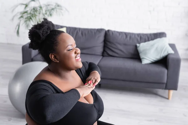 Souriant afro-américain plus taille femme en vêtements de sport exercice dans le salon — Photo de stock