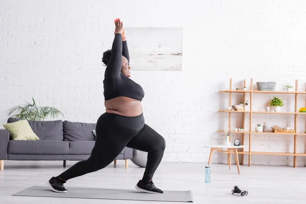 Pleine longueur de gai afro-américain plus la taille femme en tenue de sport debout dans la pose de yoga dans le salon — Photo de stock