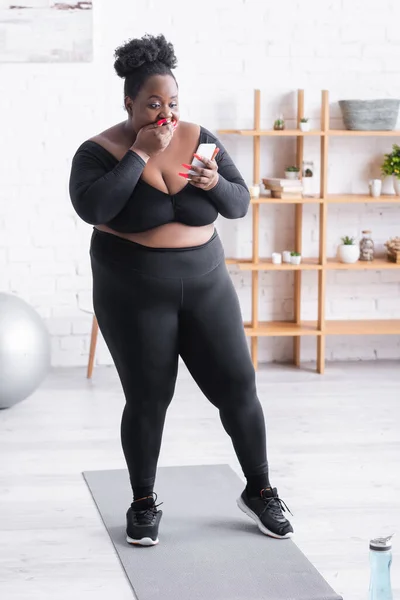 Überraschte afrikanisch-amerikanische Plus-Size-Frau in Sportbekleidung schaut aufs Smartphone und verdeckt den Mund — Stockfoto