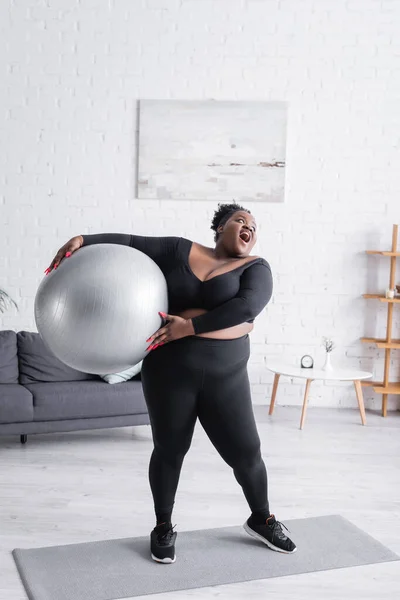 Erstaunt afrikanisch-amerikanische Plus-Size-Frau in Sportbekleidung mit Fitnessball — Stockfoto