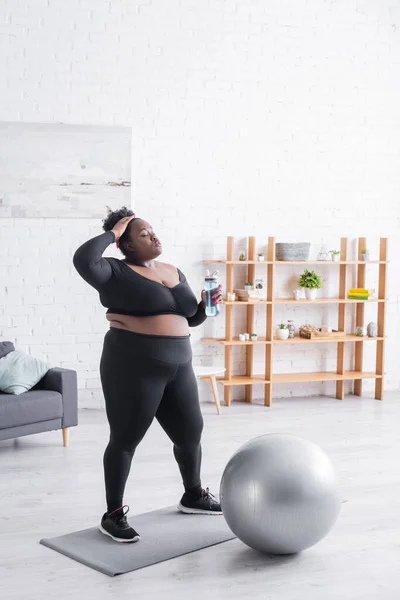 Müde afrikanisch-amerikanische Plus-Size-Frau in Sportbekleidung mit Sportflasche und lockigem Haar — Stockfoto