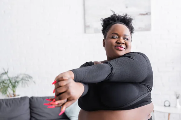Pleased african american overweight woman in sportswear exercising at home — Stock Photo