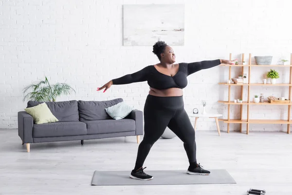 Volle Länge der zufriedenen afrikanisch-amerikanischen übergewichtigen Frau in Sportbekleidung, die zu Hause trainiert — Stockfoto