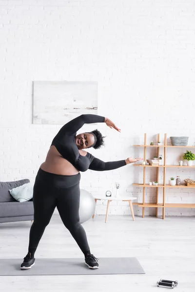 Pleine longueur de joyeuse femme afro-américaine en surpoids dans les vêtements de sport exercice à la maison — Photo de stock