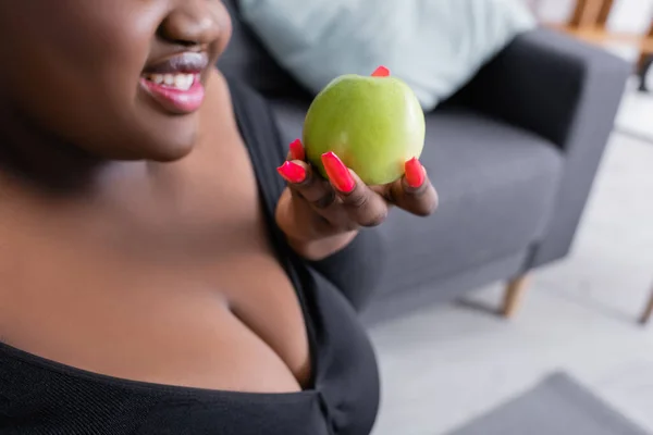 Vue recadrée de gaie afro-américaine plus la taille femme en tenue de sport tenant pomme verte — Photo de stock