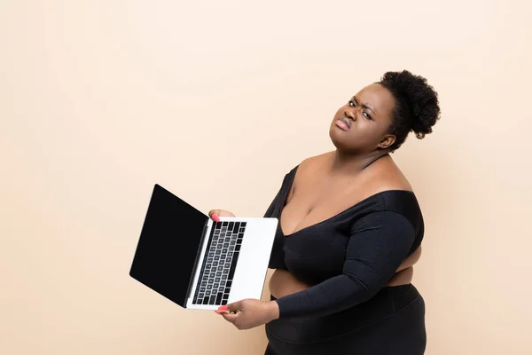 Mécontent afro-américain plus taille femme tenant ordinateur portable isolé sur beige — Photo de stock