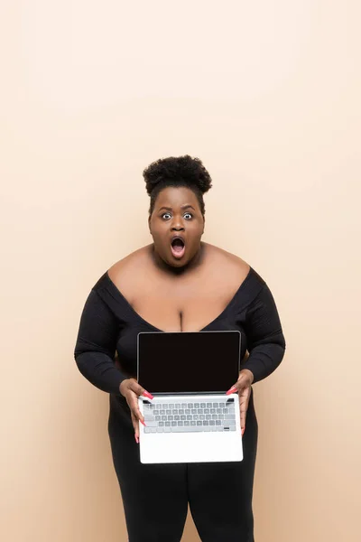 Schockierte afrikanisch-amerikanische Plus-Size-Frau hält Laptop isoliert auf beige — Stockfoto