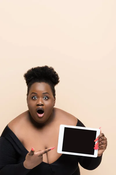 Schockierte afrikanisch-amerikanische Plus-Size-Frau hält digitales Tablet mit leerem Bildschirm isoliert auf beige — Stockfoto