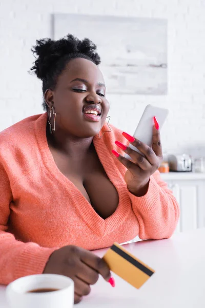 Smiling african american plus size woman holding credit card and smartphone — Stock Photo