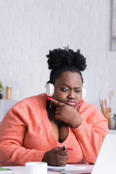 Pensive african american plus size woman in wireless headphones listening podcast — Stock Photo