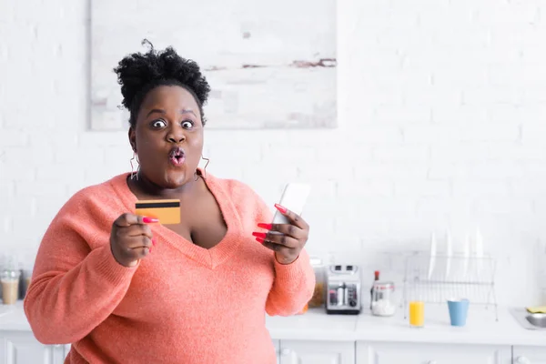 Choc afro-américain plus taille femme tenant carte de crédit et smartphone — Photo de stock