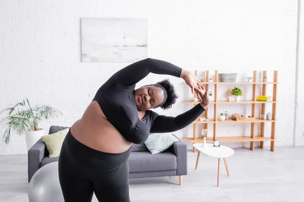 Lockige afrikanisch-amerikanische Plus-Size-Frau in Sportbekleidung beim Sport im Wohnzimmer — Stockfoto
