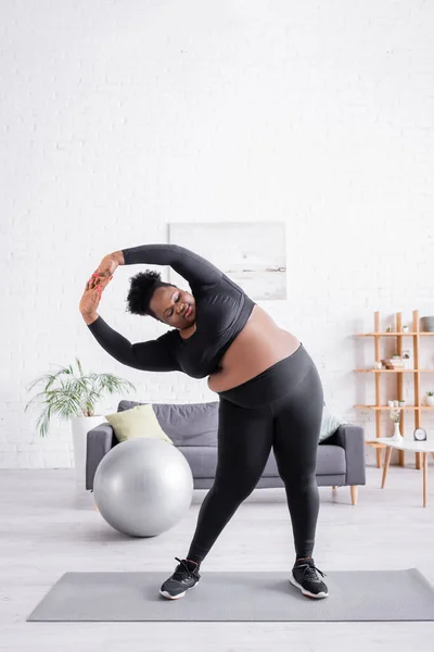 Toute la longueur de frisé afro-américain plus taille femme en vêtements de sport exercice sur tapis de fitness — Photo de stock