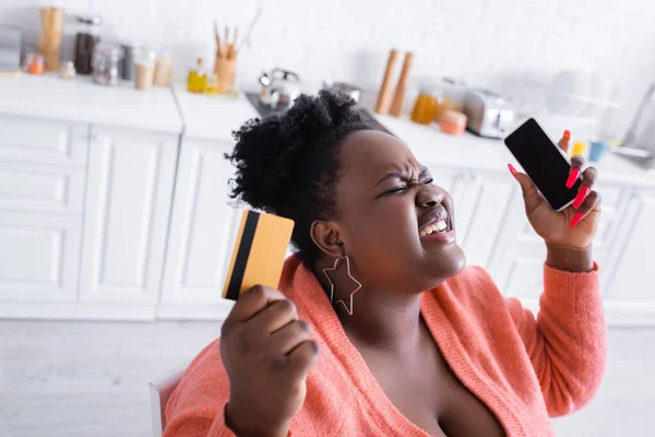 Stressed african american plus size woman holding credit card and smartphone — Stock Photo