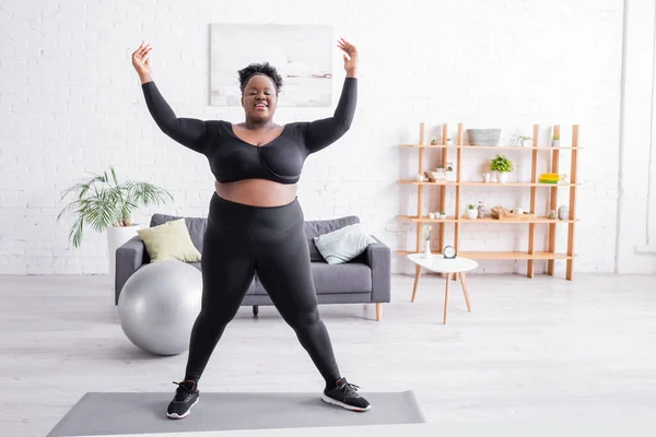 Comprimento total de mulher americana africana alegre plus size no treinamento sportswear no tapete de fitness — Fotografia de Stock