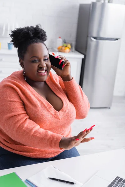 Afro-américaine plus la femme de taille parler sur smartphone, geste et regarder un ordinateur portable — Photo de stock