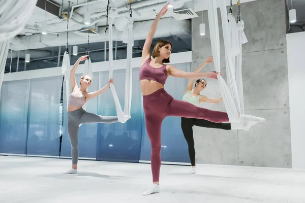 Grupo de mujeres jóvenes estirando las piernas con correas aéreas de yoga - foto de stock