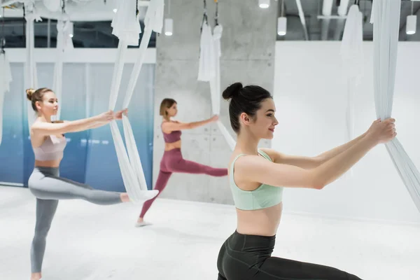 Jóvenes deportistas estirando piernas con mosca yoga hamacas - foto de stock