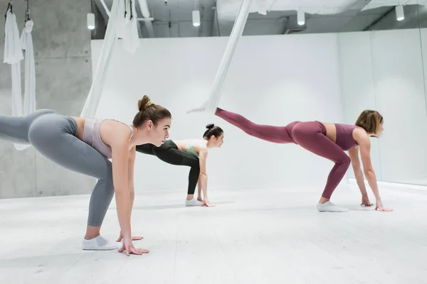 Seitenansicht junger Frauen, die sich mit Fliege-Yoga-Hängematten aufwärmen — Stockfoto