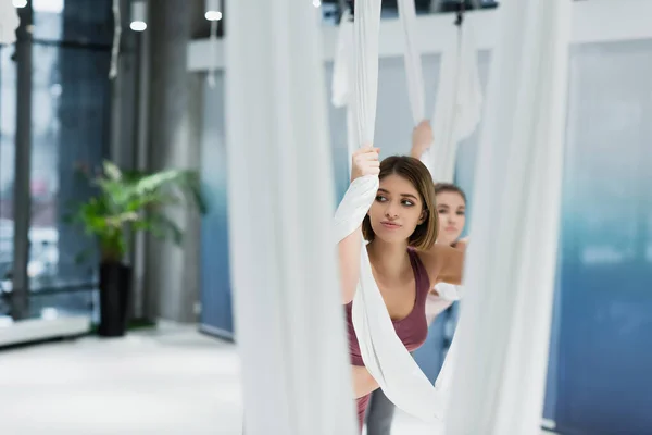 Giovane donna guardando lontano mentre si estende con amaca di yoga della mosca in primo piano offuscata — Foto stock
