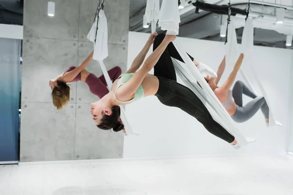 Jovens mulheres esportivas praticando ioga aérea no centro esportivo, fundo embaçado — Fotografia de Stock