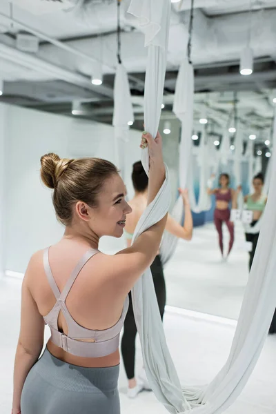 Donna allegra guardando lontano mentre si riscalda con amaca yoga aerea su sfondo sfocato — Foto stock