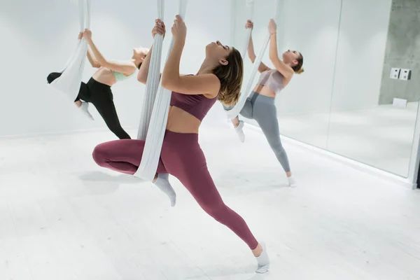 Grupo de mujeres jóvenes deportivas que se estiran en las hamacas aéreas del yoga en gimnasio - foto de stock