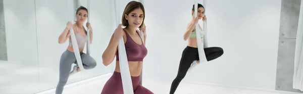 Jóvenes deportistas estirando piernas con correas aéreas de yoga, pancarta - foto de stock
