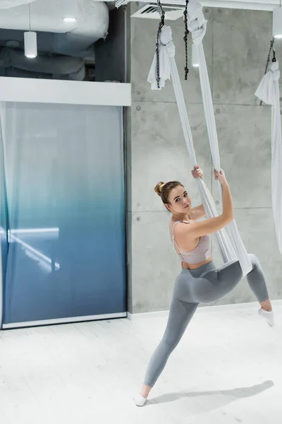 Junge Sportlerin dehnt sich mit Fliege-Yoga-Hängematte im Fitnessstudio — Stockfoto