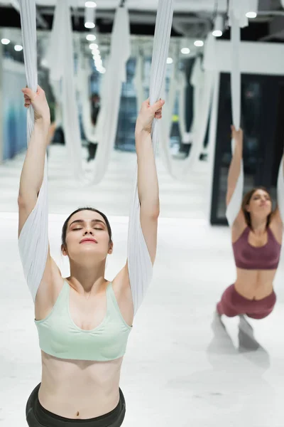 Mujer deportiva con los ojos cerrados estirándose con la correa del yoga de la mosca en fondo borroso - foto de stock