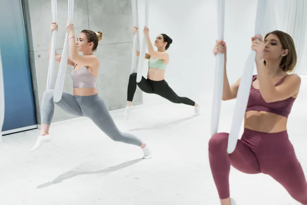 Tres jóvenes deportistas practicando yoga aéreo en primer plano borroso - foto de stock