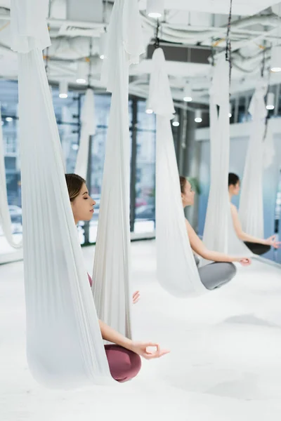 Gruppo di donne che meditano in posa loto durante la pratica di fly yoga, sfondo sfocato — Foto stock