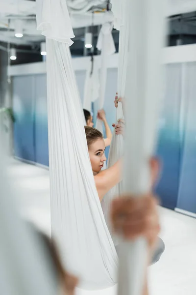 Enfoque selectivo de la mujer bonita mirando hacia otro lado mientras practica yoga aéreo - foto de stock