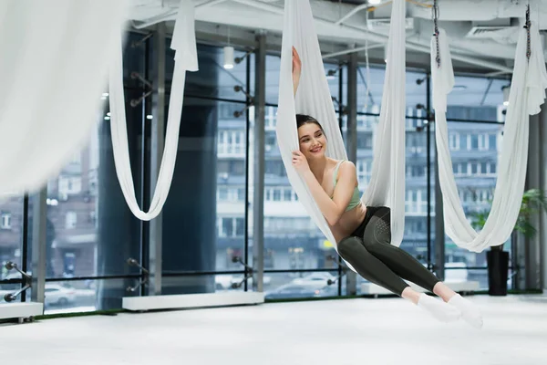 Mujer alegre que mira lejos mientras que se relaja en la hamaca del yoga de la mosca, primer plano borroso - foto de stock