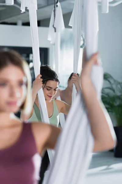Selective focus of smiling woman practicing aerial yoga on blurred foreground — Stock Photo