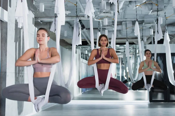 Group of sportive women meditating in lotus pose while practicing aerial yoga — Stock Photo