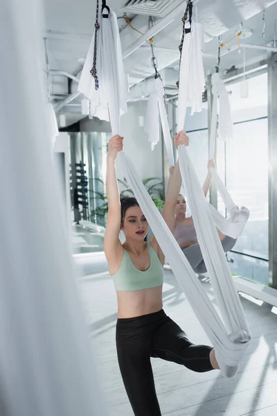 Pretty sportswoman stretching with aerial yoga hammock on blurred foreground — Stock Photo