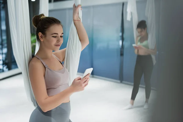 Sportiva sorridente che chiacchiera sul telefono cellulare durante l'allenamento di yoga con la mosca su sfondo sfocato — Foto stock